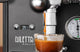 Diletta Bello+ espresso machine front panel with brew pressure gauge as espresso pours into a glass
