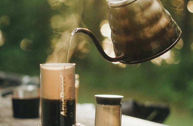 AeroPress brewing coffee outdoors with a gooseneck kettle at a campsite