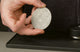 Barista holding a stainless steel espresso puck screen above a tamping mat