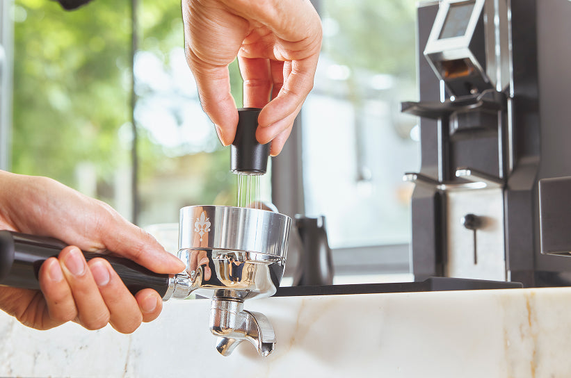 Two hands using a WDT distribution tool to stir grounds in a portafilter basket on an espresso setup