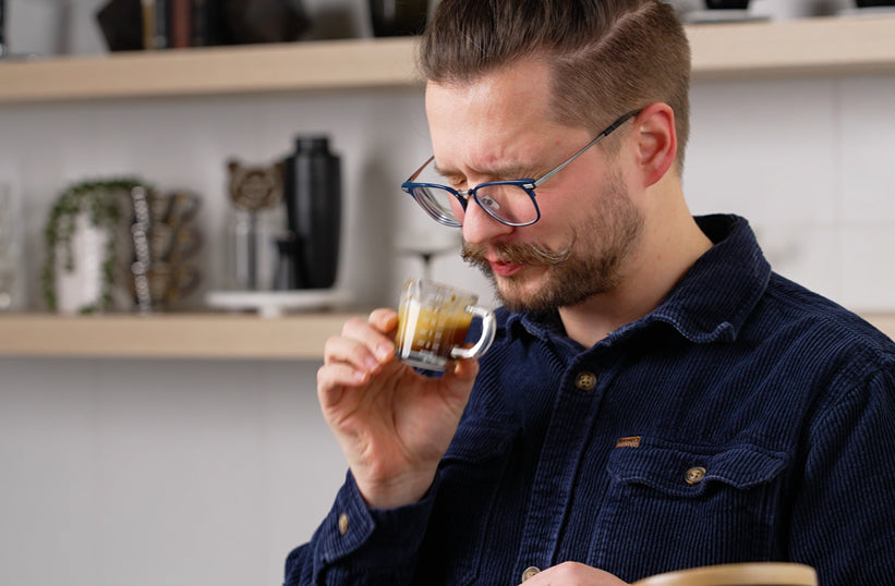 Barista smelling a shot of light roast espresso in a glass cup