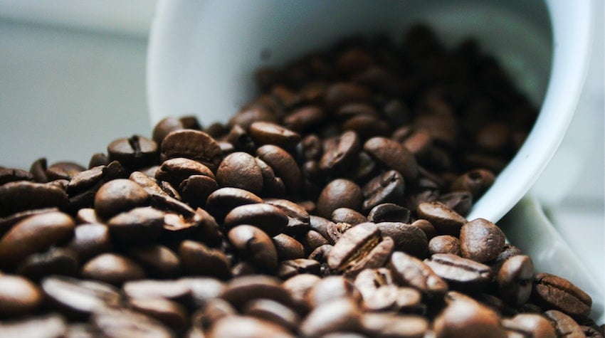 Coffee beans spilling out of a coffee cup onto a surface - Seattle Coffee Gear