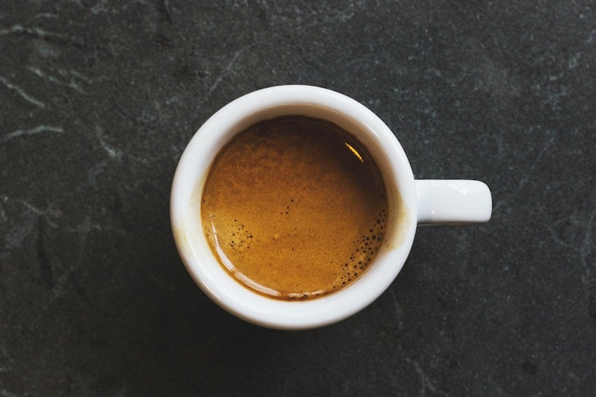 Overhead view of a coffee cup filled with a shot of espresso resting on a table surface