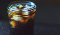 A glass jar filled with iced coffee on a dark background