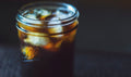 A glass jar filled with iced coffee on a dark background