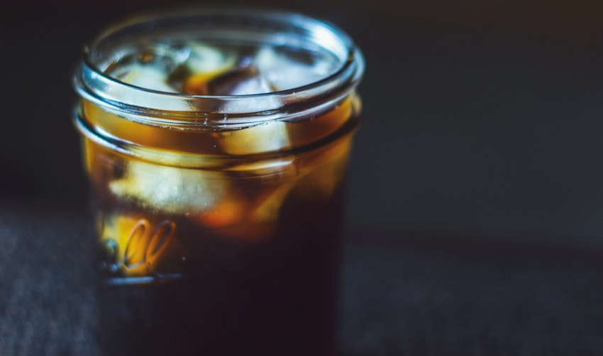 A glass jar filled with iced coffee on a dark background