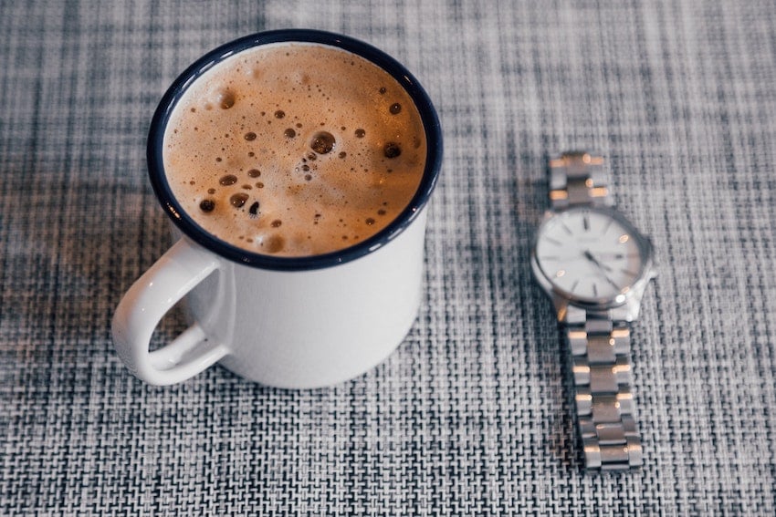 A cup of coffee topped with milk foam on a checkerboard plaid tablecloth, with a wristwatch resting beside it - Seattle Coffee Gear