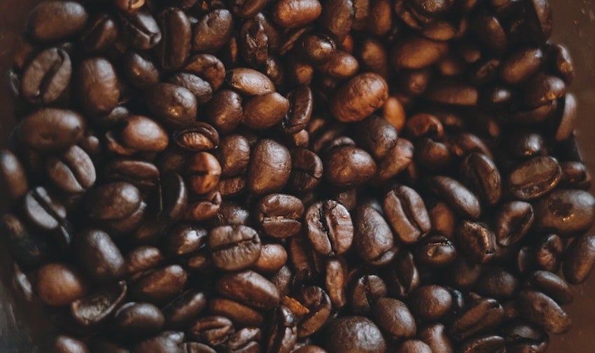 A close-up pile of roasted coffee beans spread across a dark background - Seattle Coffee Gear