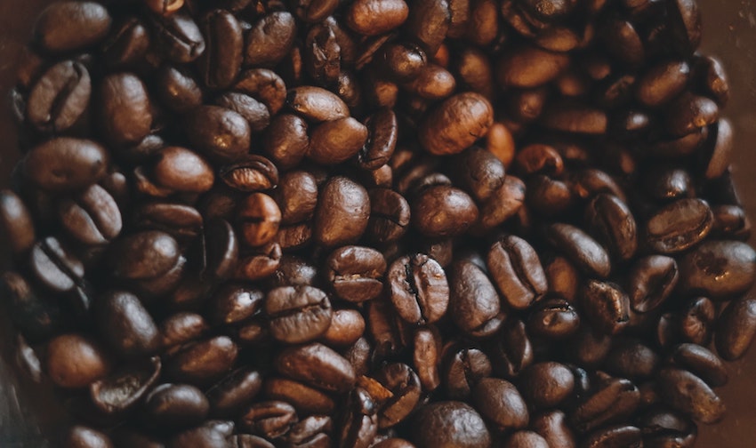 A close-up pile of roasted coffee beans spread across a dark background - Seattle Coffee Gear